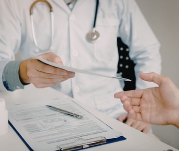 Image of a doctor handing a piece of paper to another individual. 