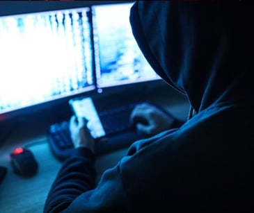 hacker on smartphone in front of computer screens