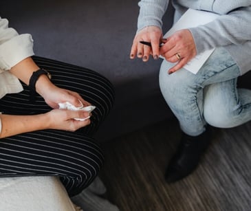 Image of someone with a notepad talking to someone holding a tissue. 