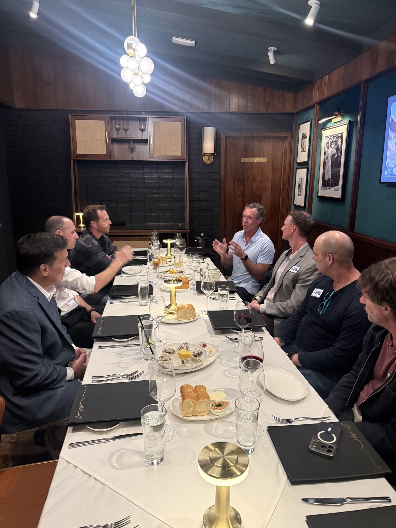 Seven people in conversation around a long dinner table in the Poolhouse at The Arthur J in Manhattan Beach | The Paubox Table: October dinner in Manhattan Beach