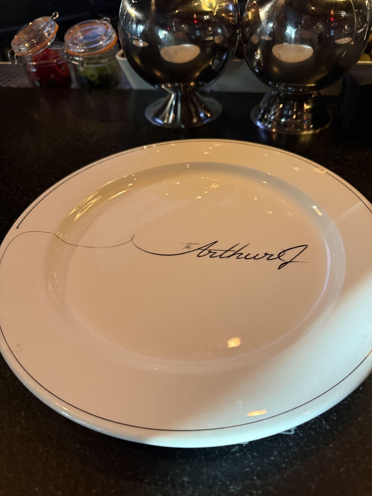 A white dinner plate with The Arthur J script logo on a dark bar top | The Paubox Table: October dinner in Manhattan Beach