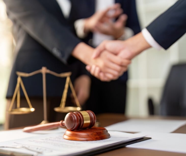 Image of two people shaking hands, near a desk that holds a scale and gavel. 
