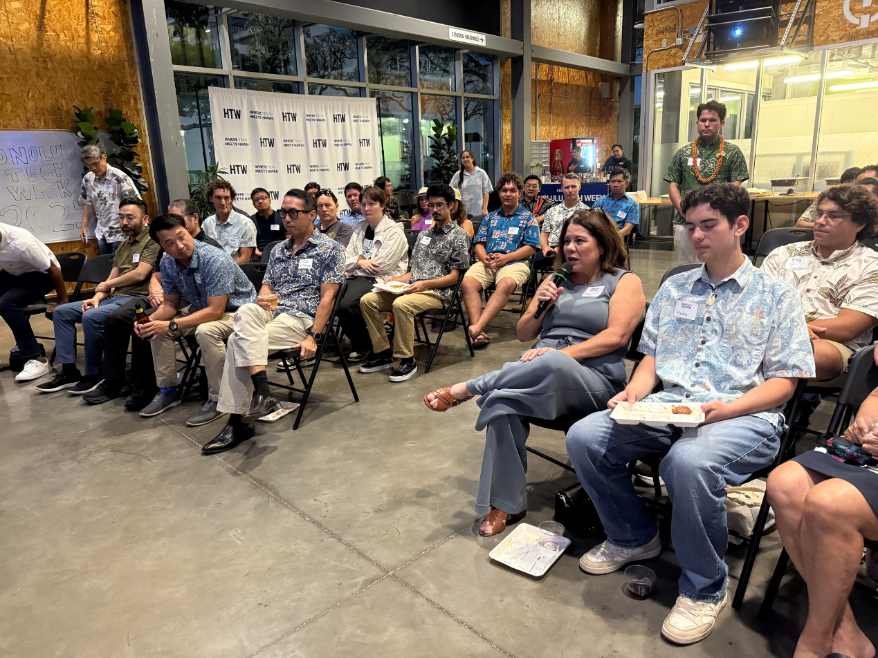 Honolulu Tech Week founder Michael Bennett (standing, wearing green aloha shirt) listens as Lori Hieger (seated, front row) poses a question to the panel