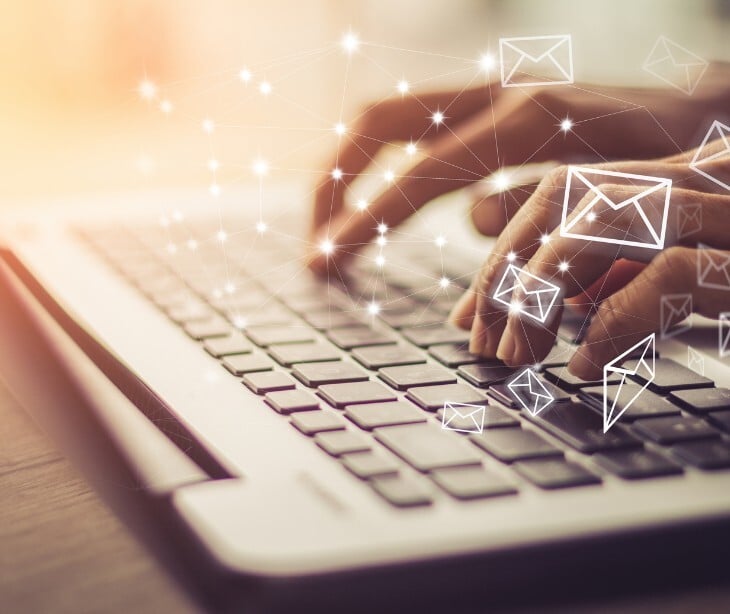 Image of someone typing on a laptop with email icons near. 