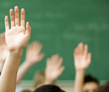 students raising hands in classroom