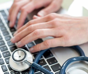 Image of a healthcare worker typing with a stethascope nearby. 
