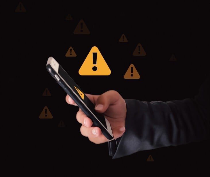 Image of someone on their phone with an alert sign. 