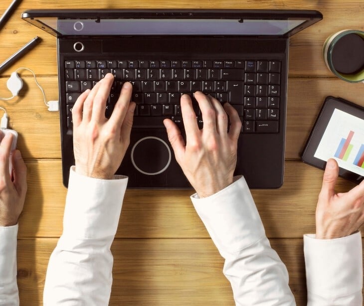 Image of someone multitasking on a computer, their desk, and phone. 
