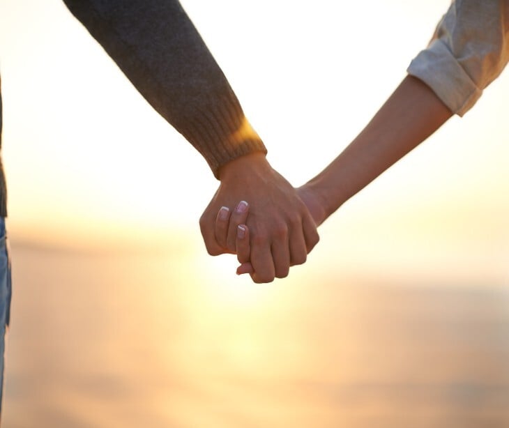 Image of two people holding hands by a sunset. 