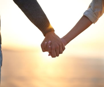 Image of two people holding hands by a sunset. 