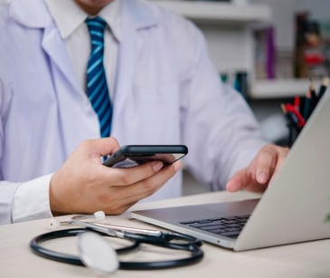 Image of a doctor on their computer and phone. 