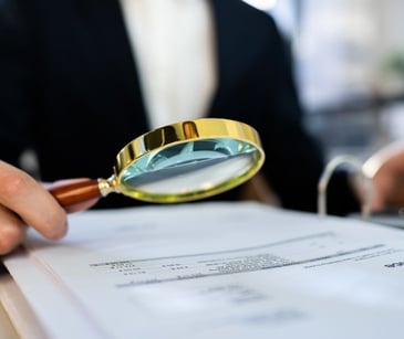 person looking at paperwork with magnifying glass