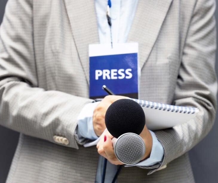 Image of a person with a press badge, notebook, and microphone. 