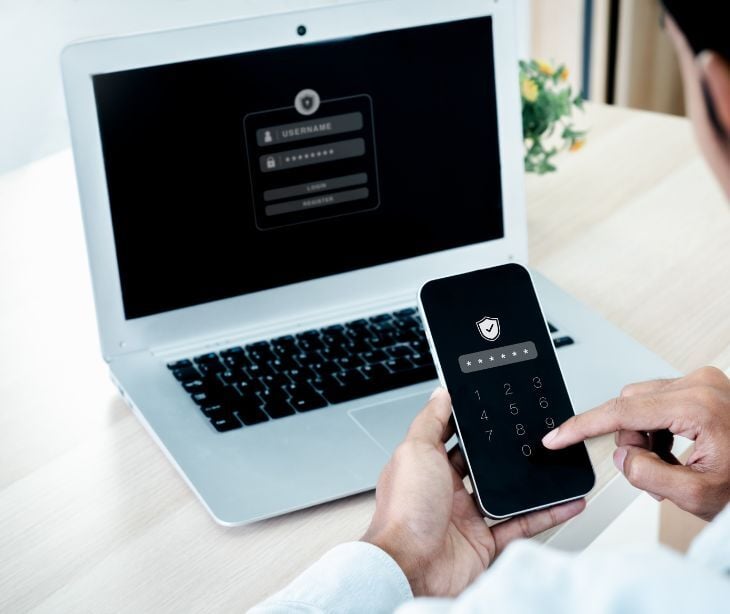 Image of someone on a phone with a computer. 