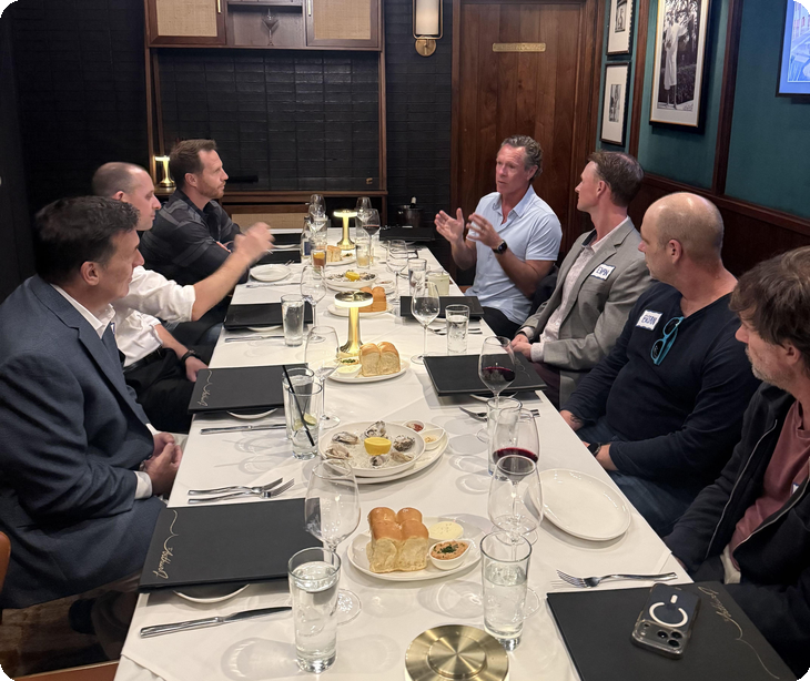 Seven people talking around a long dinner table set with bread, wine, and water glasses in the wood-paneled Poolhouse at The Arthur J in Manhattan Beach | The Paubox Table: October dinner in Manhattan Beach