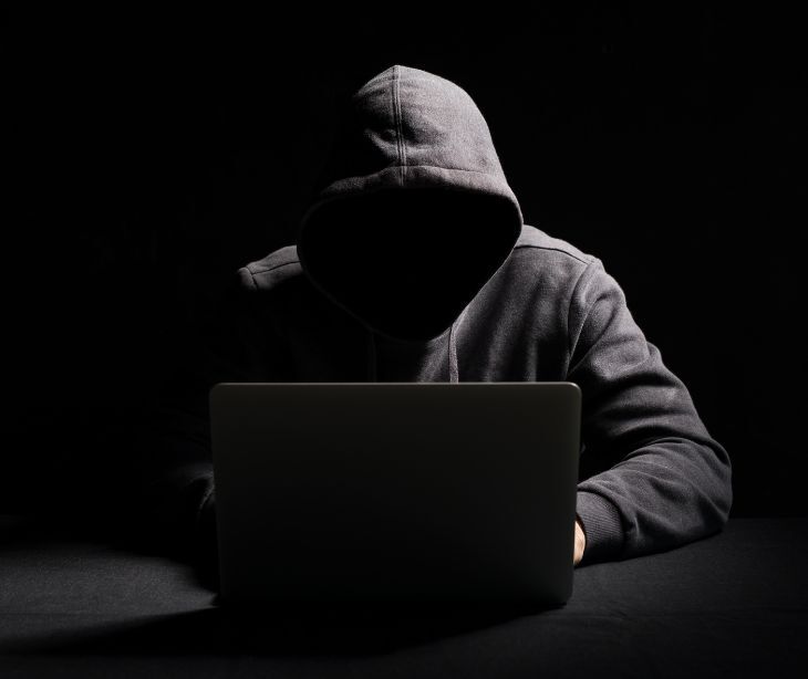 Image of a hooded figure behind a computer. 