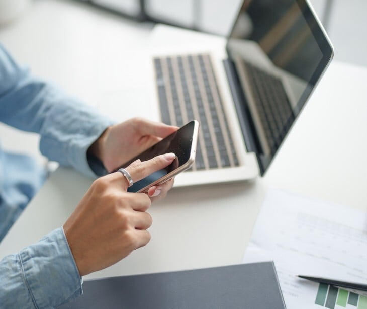 Image of someone looking at their phone with a computer nearby. 