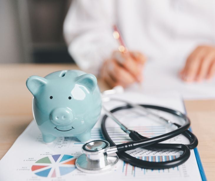 Image of a stethascope next to a piggy bank. 