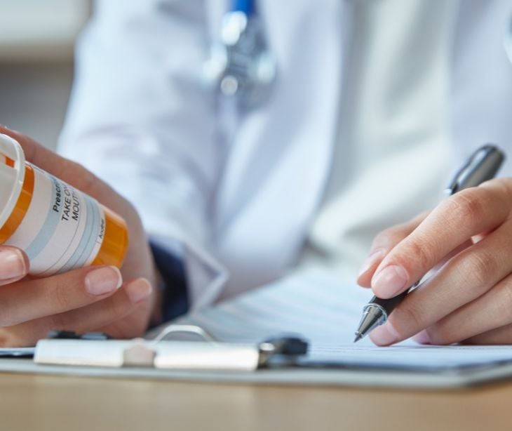 Image of a health practicioner holding a prescription bottle and writing something down. 