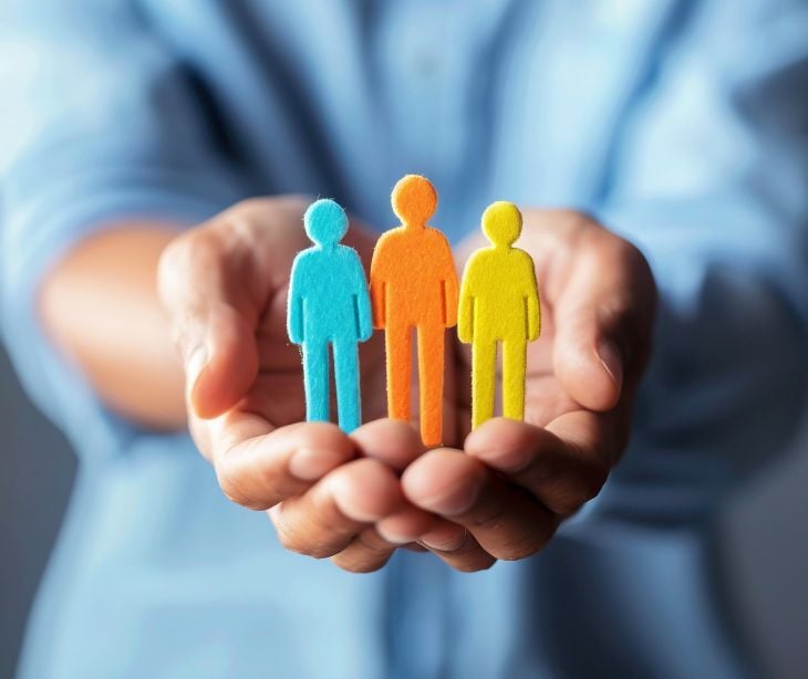 Image of a hand holding small cardboard cutouts of people. 